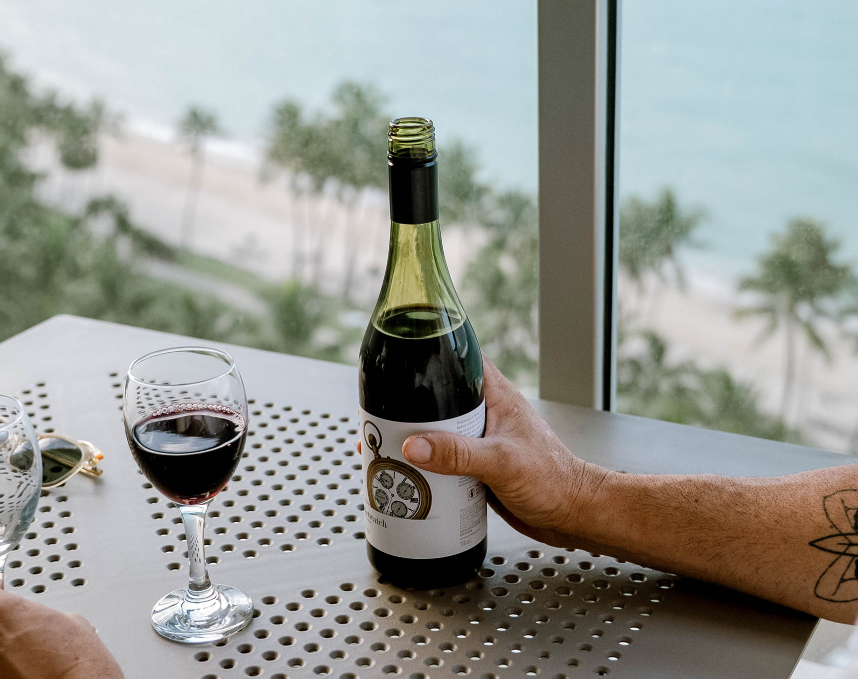A couple enjoying red wine on a private balcony overlooking Catseye Beach and palm trees at Whitsunday Apartments Hamilton Island
